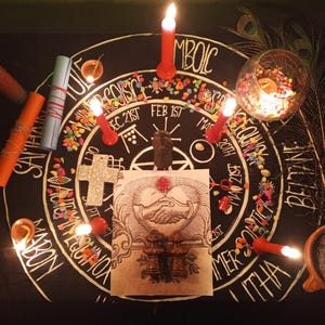 Puede incluir: Una configuraci&oacute;n de altar m&iacute;stico con velas, pergaminos y una ilustraci&oacute;n central de manos entrelazadas. El altar incluye una cruz, un cuenco de vidrio con piedras de colores y plumas de pavo real. El texto en el altar incluye las palabras: SAMHAIN, ITHA y BELTANE.