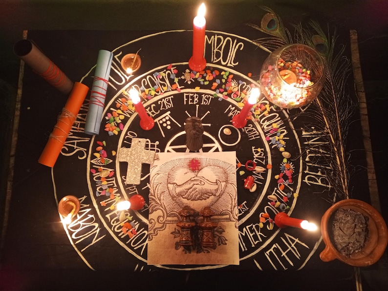 Puede incluir: Una configuraci&oacute;n de altar m&iacute;stico con velas, pergaminos y una ilustraci&oacute;n central de manos entrelazadas. El altar incluye una cruz, un cuenco de vidrio con piedras de colores y plumas de pavo real. El texto en el altar incluye las palabras: SAMHAIN, ITHA y BELTANE.