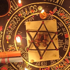 K&ouml;nnte beinhalten: Eine rituelle Szene mit einem zentralen sternf&ouml;rmigen Design mit zwei Figuren, umgeben von Kerzen und Text. Das Design befindet sich auf einer dunklen Oberfl&auml;che mit zus&auml;tzlichem Text und Symbolen, und ein kleiner Tonkrug ist sichtbar.