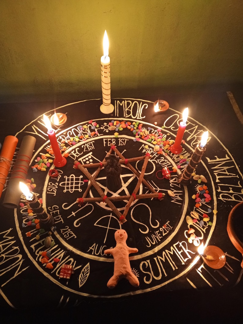 Puede incluir: Un altar circular negro con letras y s&iacute;mbolos blancos, rodeado de velas encendidas. En el centro hay una disposici&oacute;n de estrella y palos, con una peque&ntilde;a figura de arcilla en la parte inferior. Se ven piedras de colores y el texto "IMBOLC".