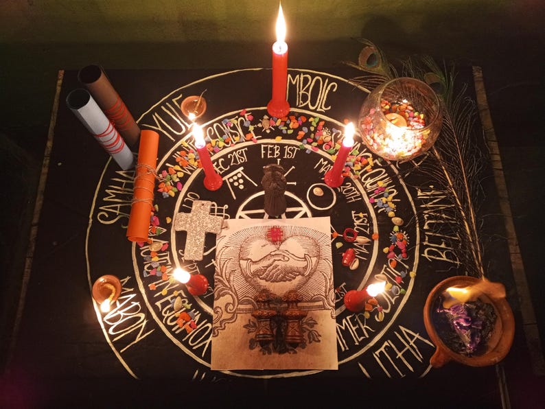 Puede incluir: Un altar m&iacute;stico con una superficie negra, adornado con velas, una cruz decorativa y una ilustraci&oacute;n central de manos entrelazadas. El altar est&aacute; decorado con cuentas de colores y plumas de pavo real, creando un ambiente espiritual. El texto en el altar incluye las palabras: YULE, IMBOLC, COISCE, SAMHAIN, MABON, BELTANE, y LITHA.