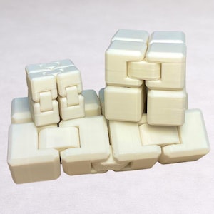 May include: A cream-colored, interlocking puzzle toy composed of multiple cube-shaped pieces. The pieces are connected by hinges, allowing for flexible movement and manipulation. The toy is designed to be assembled and disassembled.