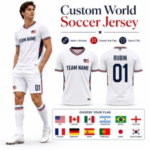 Può includere: Maglia da calcio bianca personalizzata con finiture rosse e blu, con la scritta "TEAM NAME" e la bandiera americana. La maglia è esposta con pantaloncini e calzini abbinati. L'immagine mostra anche il retro della maglia con il nome "RUBIN" e il numero "01".