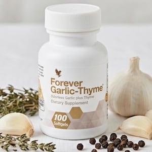Könnte beinhalten: Eine weiße Flasche des Nahrungsergänzungsmittels "Forever Garlic-Thyme" mit weißem Deckel. Die Flasche befindet sich neben einem Knoblauchkopf, Knoblauchzehen, Thymianzweigen und Pfefferkörnern. Die Flasche enthält 100 Softgels.