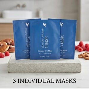 May include: Three blue individual face masks are displayed on a gray stone block. Each packet has the words "aloe bio-cellulose mask" and the Forever logo. Raspberries, almonds, and pastries are in the background.