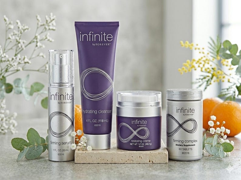 K&ouml;nnte beinhalten: Eine Auswahl an Hautpflegeprodukten, darunter ein Serum, ein Reiniger, eine Creme und ein Nahrungserg&auml;nzungsmittel. Die Produkte sind in silber- und lilafarbenen Verpackungen mit dem Wort "infinite" und einem stilisierten Unendlichkeitszeichen gehalten. Das Bild enth&auml;lt auch Orangen und Blumengestecke.