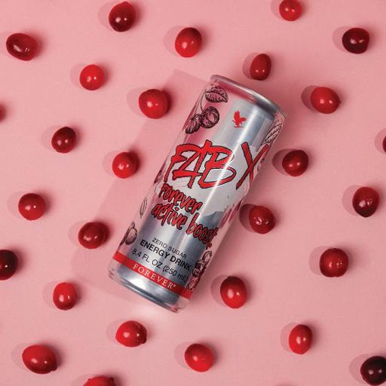 May include: A silver energy drink can with red and white text, surrounded by red berries on a pink background. The can reads "FAB X Forever active boost" and "Zero Sugar Energy Drink 250 ml".