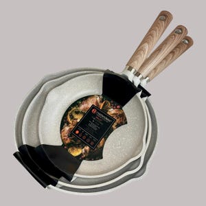 May include: A set of three nested skillets with a light gray speckled non-stick interior and light brown wood-grain patterned handles. A black paper label is wrapped around the pans, featuring the text Masterclass Skillet 20 cm.