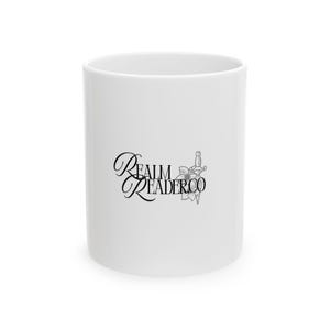 May include: A white ceramic mug featuring a black graphic design on the front. The design includes the text REALM READER CO in a stylized serif font, accompanied by a detailed line art illustration of a flower and a dagger positioned vertically.