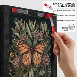 May include: A framed art print featuring a monarch butterfly with orange and black wings, surrounded by green foliage and pink flowers. The frame is black. The image shows the steps for easy, no-damage installation using nano tape.