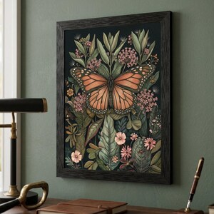 May include: A framed art print featuring a monarch butterfly with orange and black wings, centered amidst lush green foliage and pink flowers. The artwork is set against a dark background, framed in a dark wood.