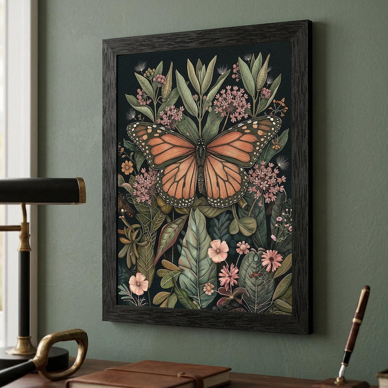 May include: A framed art print featuring a monarch butterfly with orange and black wings, centered amidst lush green foliage and pink flowers. The artwork is set against a dark background, framed in a dark wood.