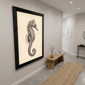 May include: A framed black and white seahorse art print. The seahorse is detailed with shading and texture, set against a cream-colored background. The frame is a thick, dark wood, adding a classic touch to the artwork.