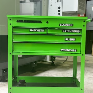 May include: A bright lime green metal tool cart with four drawers and a bottom shelf. The cart features black labels reading US GENERAL, SOCKETS, RATCHETS, EXTENSIONS, PLIERS, and WRENCHES. It is mounted on four black swivel casters for mobility.