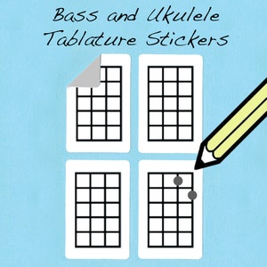 May include: Four white stickers with black grid lines, designed for writing bass and ukulele tablature. One sticker has two black dots on the grid.
