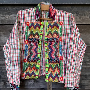 May include: A long-sleeved jacket featuring a white base with a red, green, and blue plaid pattern. The front panels and collar display vibrant, multi-colored zigzag embroidery and floral motifs, accented by bright neon green trim along the edges.