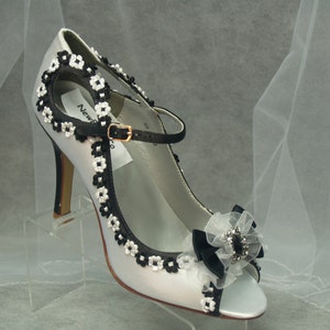 May include: White satin bridal shoes with black floral trim and a black bow with a rhinestone embellishment.
