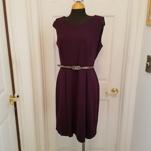 May include: A sleeveless, purple dress with a snakeskin-patterned belt. The dress has a round neckline and a straight skirt.