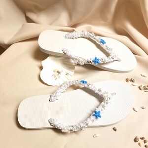 May include: White flip flops with white crocheted straps decorated with blue starfish and white beads.