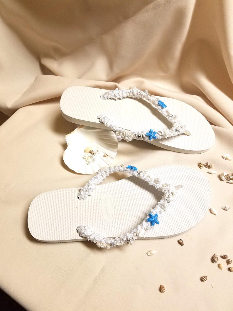 May include: White flip flops with white crocheted straps decorated with blue starfish and white beads.