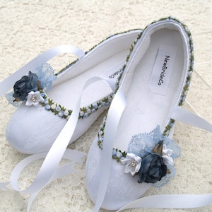 May include: White satin bridal shoes with blue and green floral embroidery and lace accents. The shoes have satin ribbons and a label that reads "NewBrideCo."
