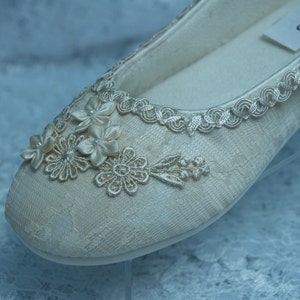 Puede incluir: Un par de zapatos de novia de sat&eacute;n marfil con delicados encajes y adornos florales. Los zapatos tienen un dise&ntilde;o simple y elegante y son perfectos para una boda.