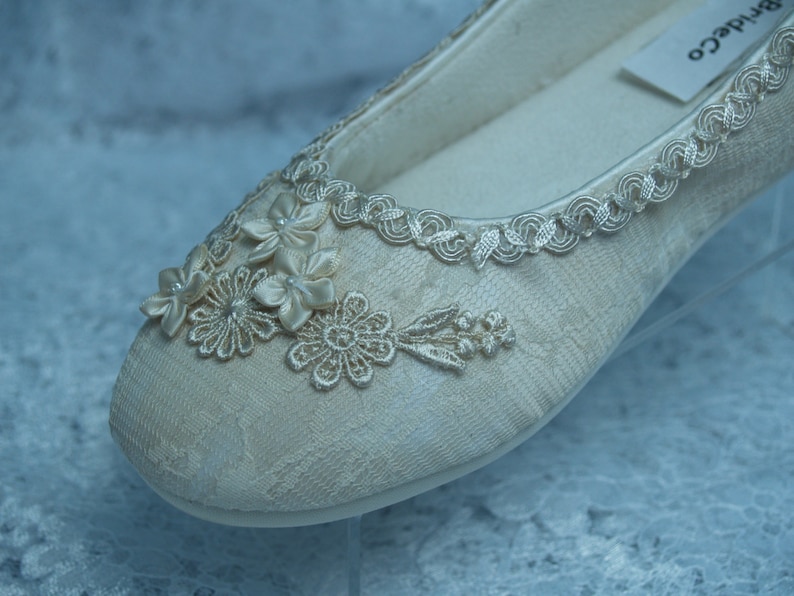 Puede incluir: Un par de zapatos de novia de sat&eacute;n marfil con delicados encajes y adornos florales. Los zapatos tienen un dise&ntilde;o simple y elegante y son perfectos para una boda.