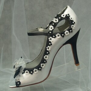 May include: White satin peep-toe heels with black and white floral embroidery and a black bow accent.