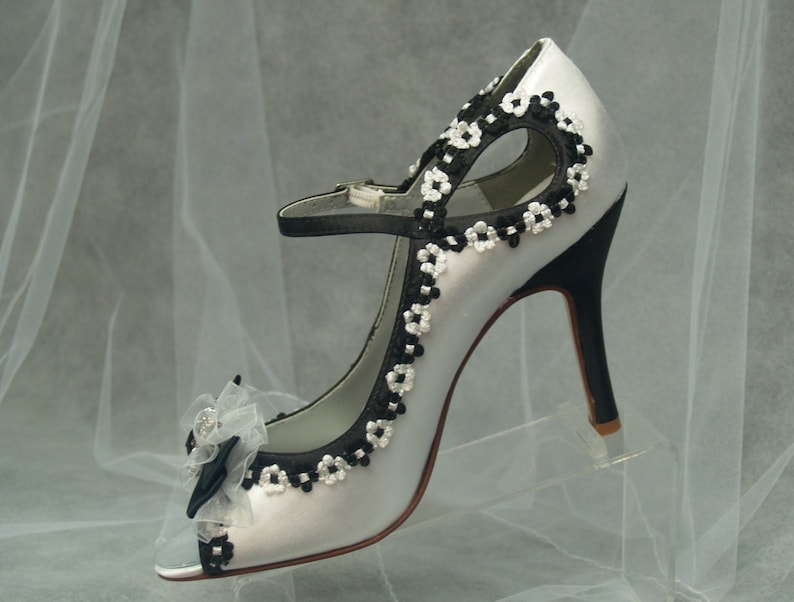 May include: White satin peep-toe heels with black and white floral embroidery and a black bow accent.