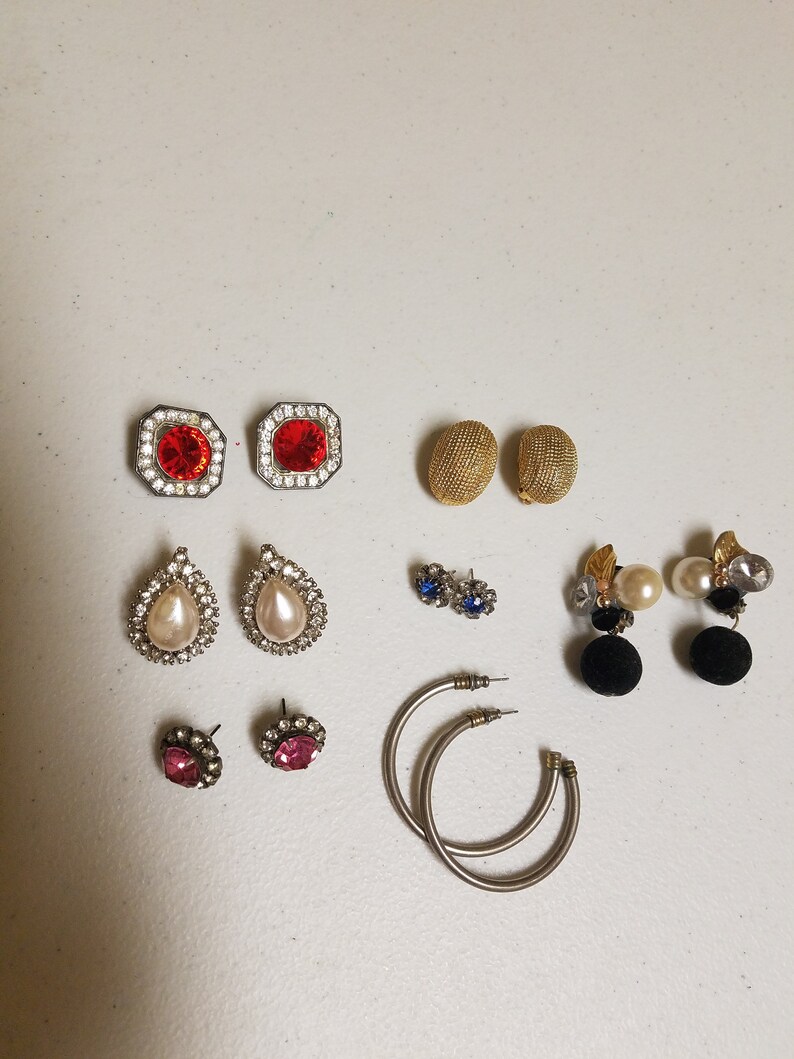 May include: Assortment of earrings in various styles and colors, including red, pink, blue, and white. Some earrings feature pearl accents, while others have geometric designs.