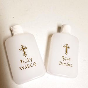 May include: Two white plastic bottles with gold crosses and text. The bottle on the left says "holy water" and the bottle on the right says "Agua Bendita".