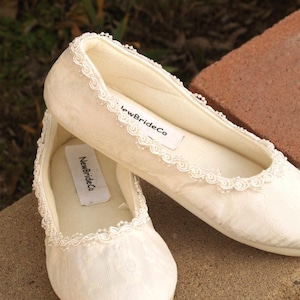 May include: A pair of white satin bridal slippers with lace trim and the text "NewBrideCo" on the inside of each shoe.