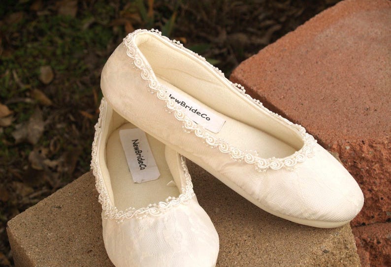 May include: A pair of white satin bridal slippers with lace trim and the text "NewBrideCo" on the inside of each shoe.