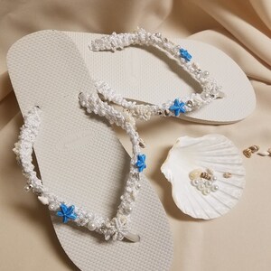 May include: White flip flops with white crocheted straps decorated with blue starfish and white pearls.
