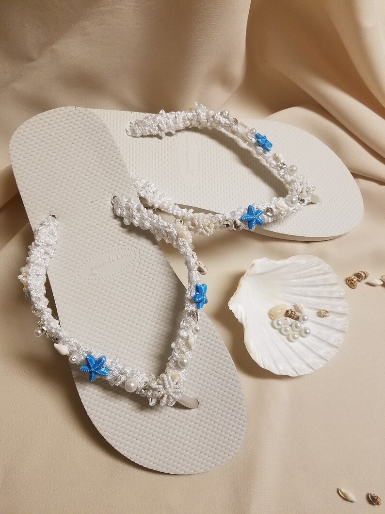 May include: White flip flops with white crocheted straps decorated with blue starfish and white pearls.