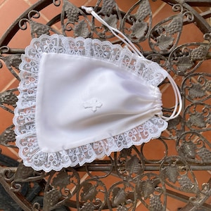 May include: White satin drawstring bag with a lace trim and a small embroidered cross. The bag is sitting on a decorative metal surface.
