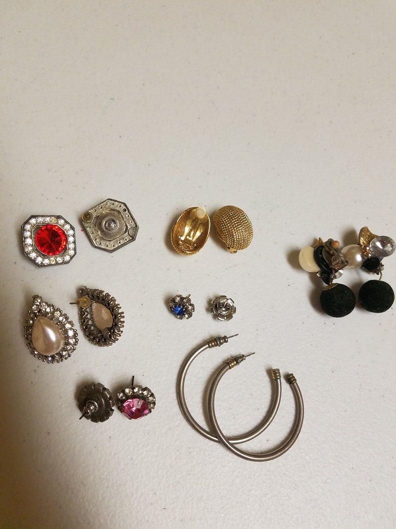 May include: Assortment of earrings in various styles and colors, including silver, gold, and black. Some earrings feature rhinestones, pearls, and other decorative elements.