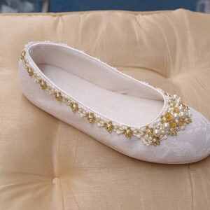 May include: White satin bridal shoes with a pearl and gold bead embellishment.