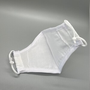 May include: White face mask with adjustable ear loops. The mask is made of a lightweight fabric and features a contoured design for a comfortable fit. The mask is designed to cover the nose and mouth.