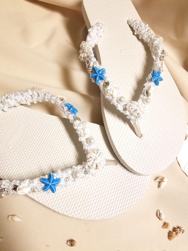 May include: White flip flops decorated with white crocheted straps, white beads, and blue starfish charms.
