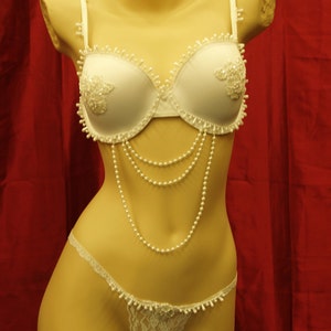 Può includere: Completo intimo in pizzo bianco con dettagli in perle. Il reggiseno presenta un delicato motivo floreale e la mutandina abbinata ha un bordo smerlato.