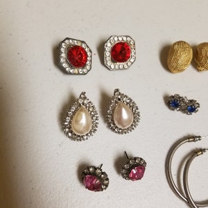 May include: Assortment of earrings with various styles and colors, including red, pink, white, and blue stones. There are also two gold hoop earrings.