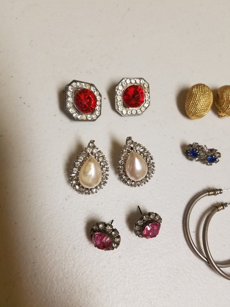 May include: Assortment of earrings with various styles and colors, including red, pink, white, and blue stones. There are also two gold hoop earrings.