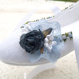 May include: White lace ballet flats with a blue and white flower embellishment. The flower is made of fabric and has a pearl in the center.