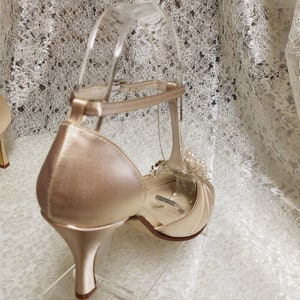 May include: A pair of ivory satin heeled shoes with a delicate ankle strap and a pearl embellishment.