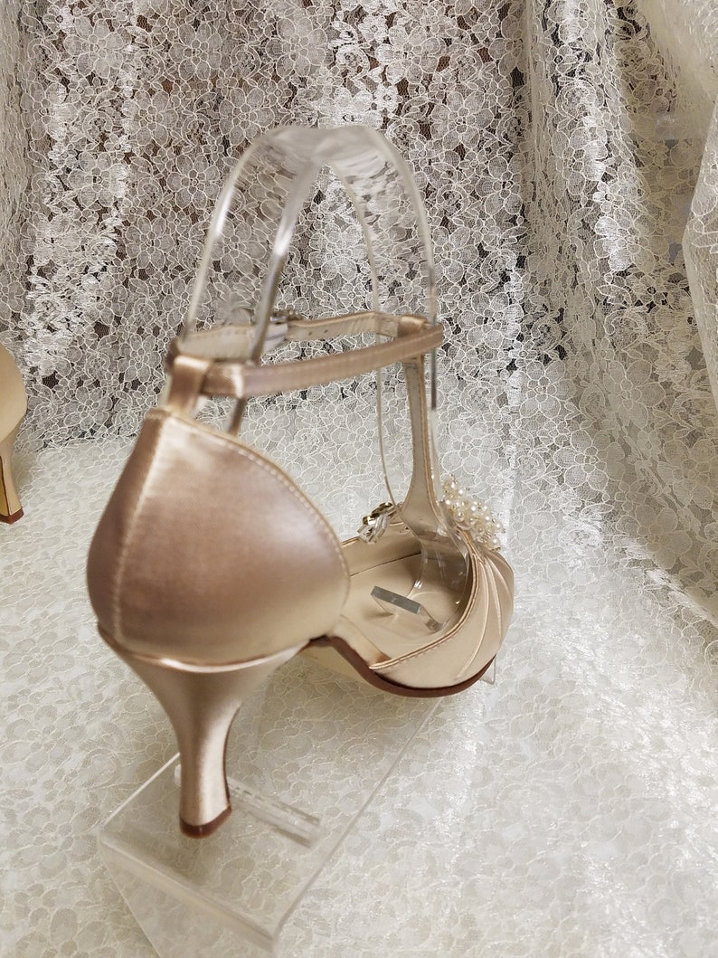 May include: A pair of ivory satin heeled shoes with a delicate ankle strap and a pearl embellishment.