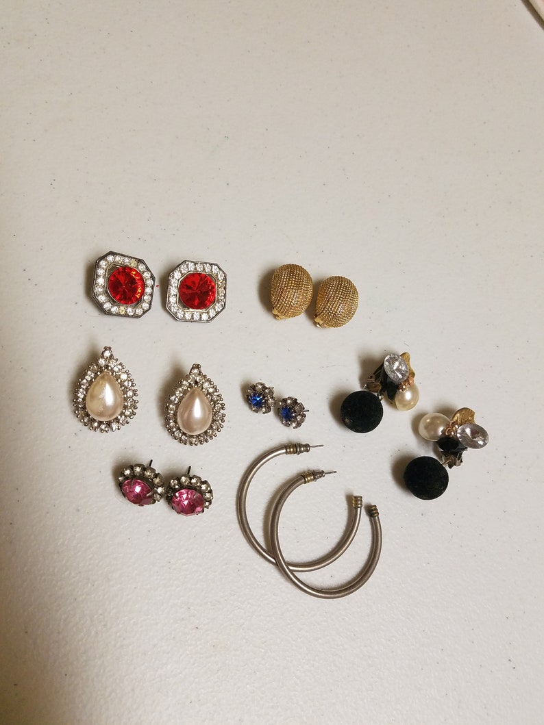 May include: Assortment of vintage earrings in various styles and colors, including red, blue, pink, white, and gold. The earrings feature different shapes, such as teardrop, round, and square.