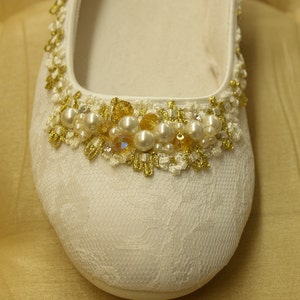 May include: White satin bridal shoe with a gold and pearl embellishment around the toe.