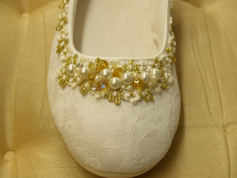 May include: White satin bridal shoe with a gold and pearl embellishment around the toe.