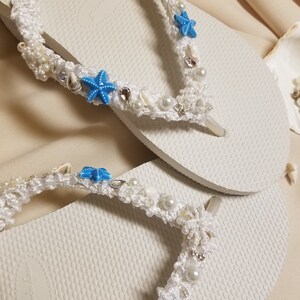 May include: White flip flops with a white crocheted strap decorated with blue starfish, white pearls, and silver beads.